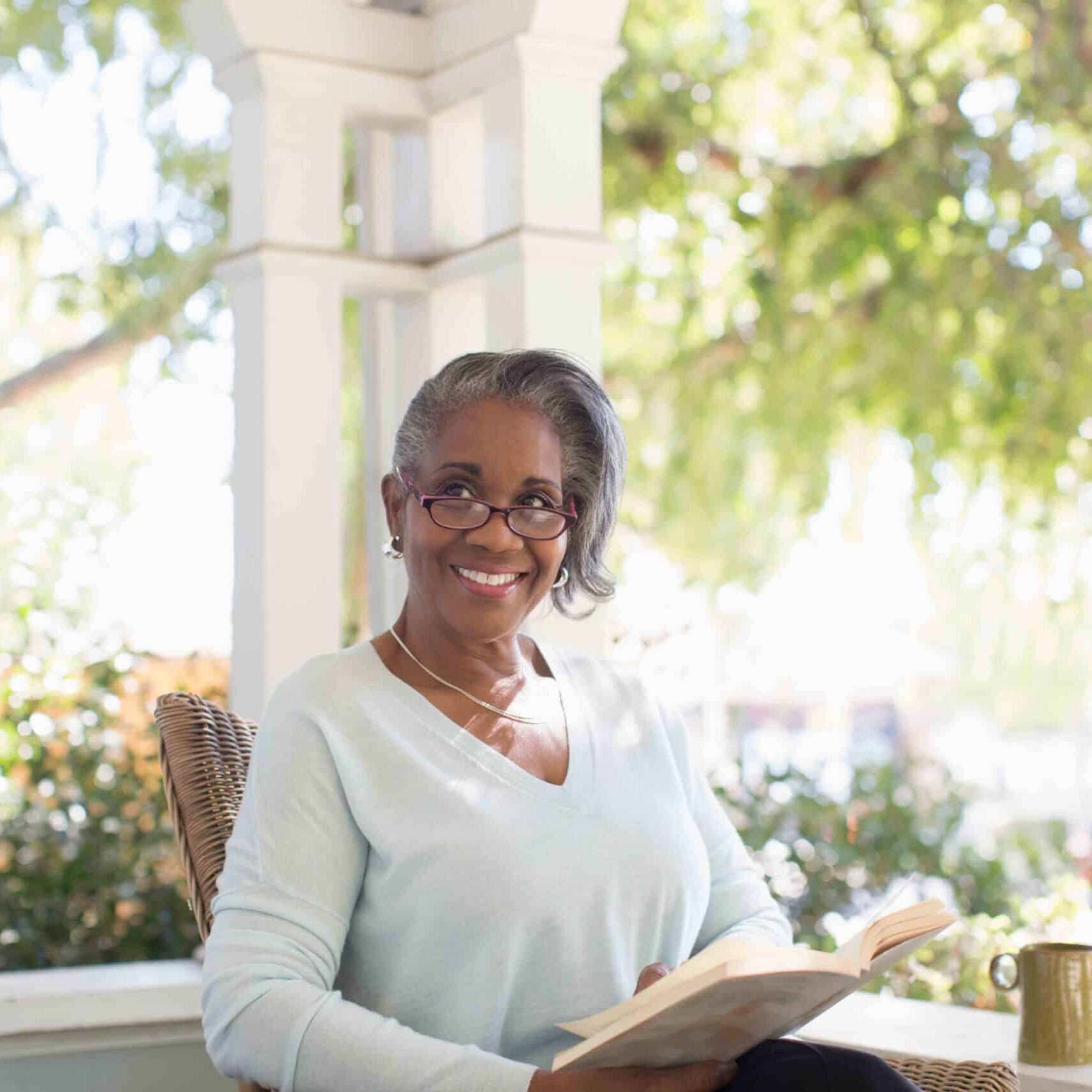 Portrait happy senior woman reading book on sunny porch